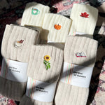 Load image into Gallery viewer, Set of beige socks with embroidered designs on a patterned surface
