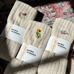 Load image into Gallery viewer, Three pairs of beige socks with &#39;garden of daisies&#39; labels on a textured surface.
