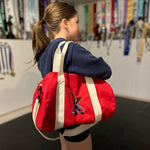 Load image into Gallery viewer, Person holding a red duffel bag with a logo in an indoor setting
