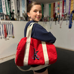 Load image into Gallery viewer, Person holding a red duffel bag with a logo in an indoor setting with flags on the wall.
