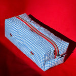 Load image into Gallery viewer, Blue checkered toiletry bag with a red zipper on a red background
