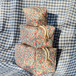 Load image into Gallery viewer, Stack of floral-patterned fabric cosmetic bgs on a checkered fabric background
