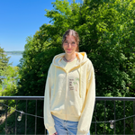 Charger l'image dans la galerie, Person wearing a light-colored hoodie with a scenic background of trees and water.
