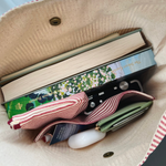 Load image into Gallery viewer, Open beige bag with books, ribbons, and a white object inside
