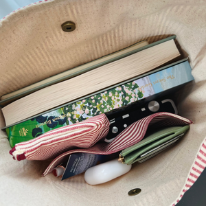 Open beige bag with books, ribbons, and a white object inside