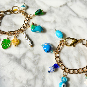 Gold charm bracelets with colorful beads on a marble surface