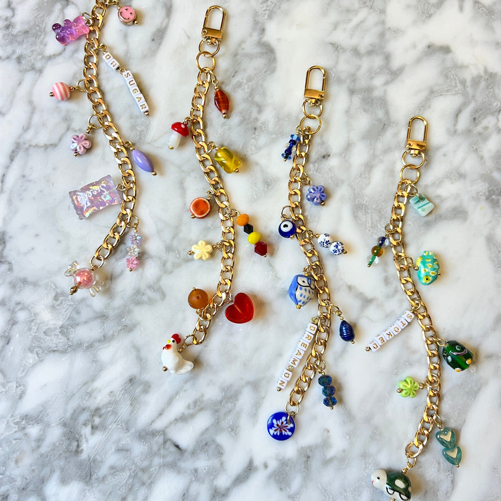 Gold charm bracelets with colorful beads on a marble surface