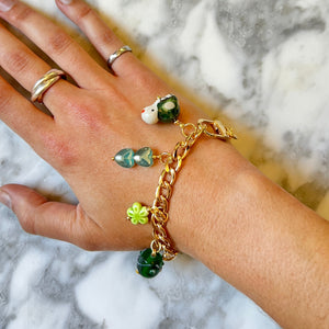Hand wearing gold bracelet with green beads on a marble background