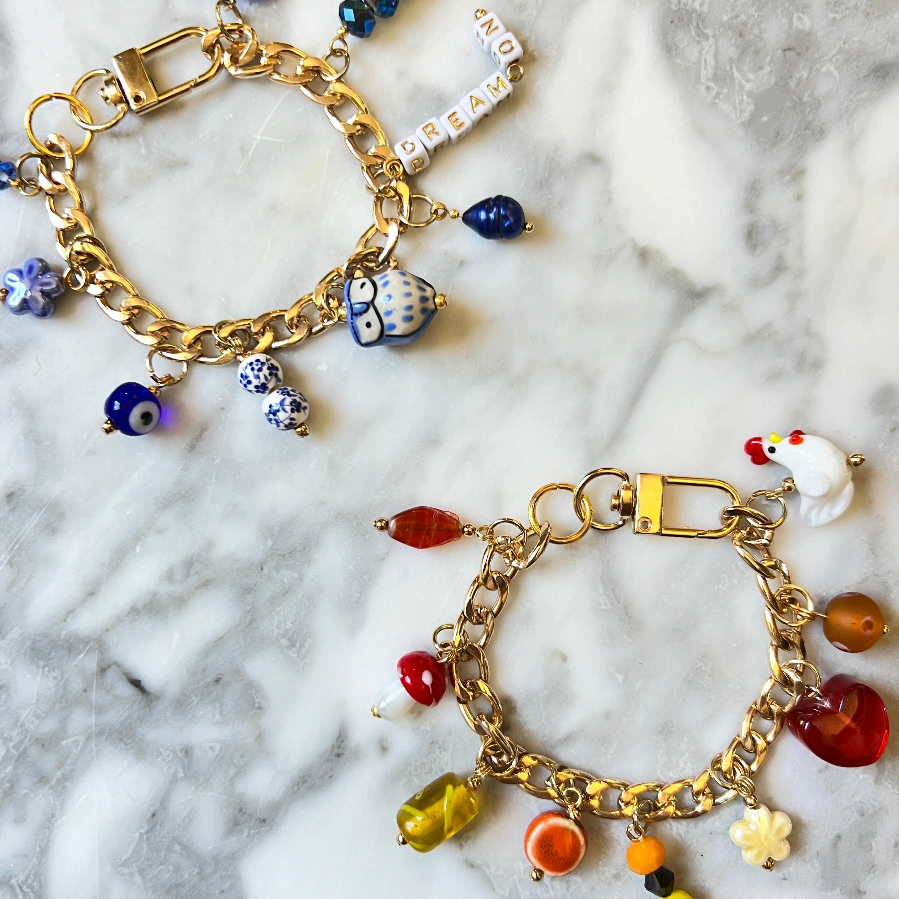 Two gold charm bracelets on a marble surface