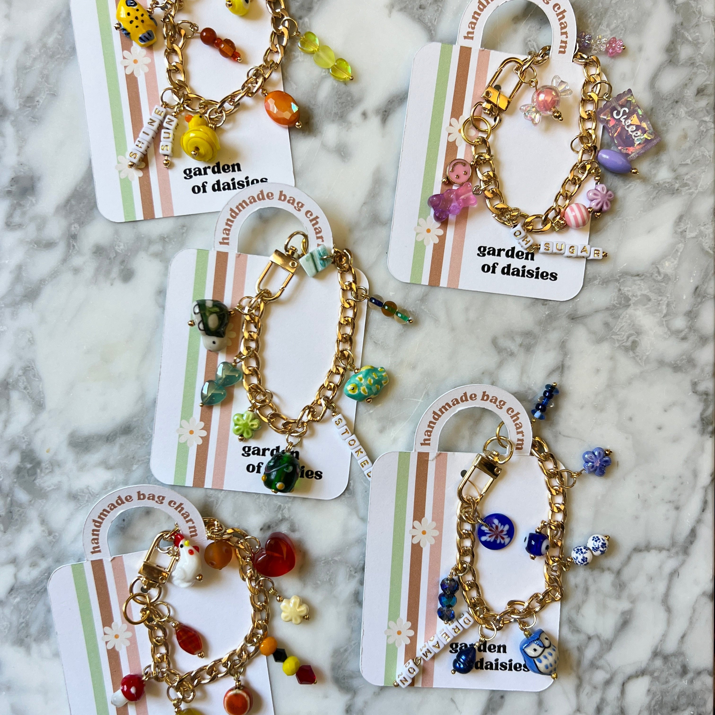 Set of five gold bracelets with colorful beads on cards labeled 'Garden of Daisies' against a marble background.
