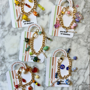 Set of five gold bracelets with colorful beads on cards labeled 'Garden of Daisies' against a marble background.