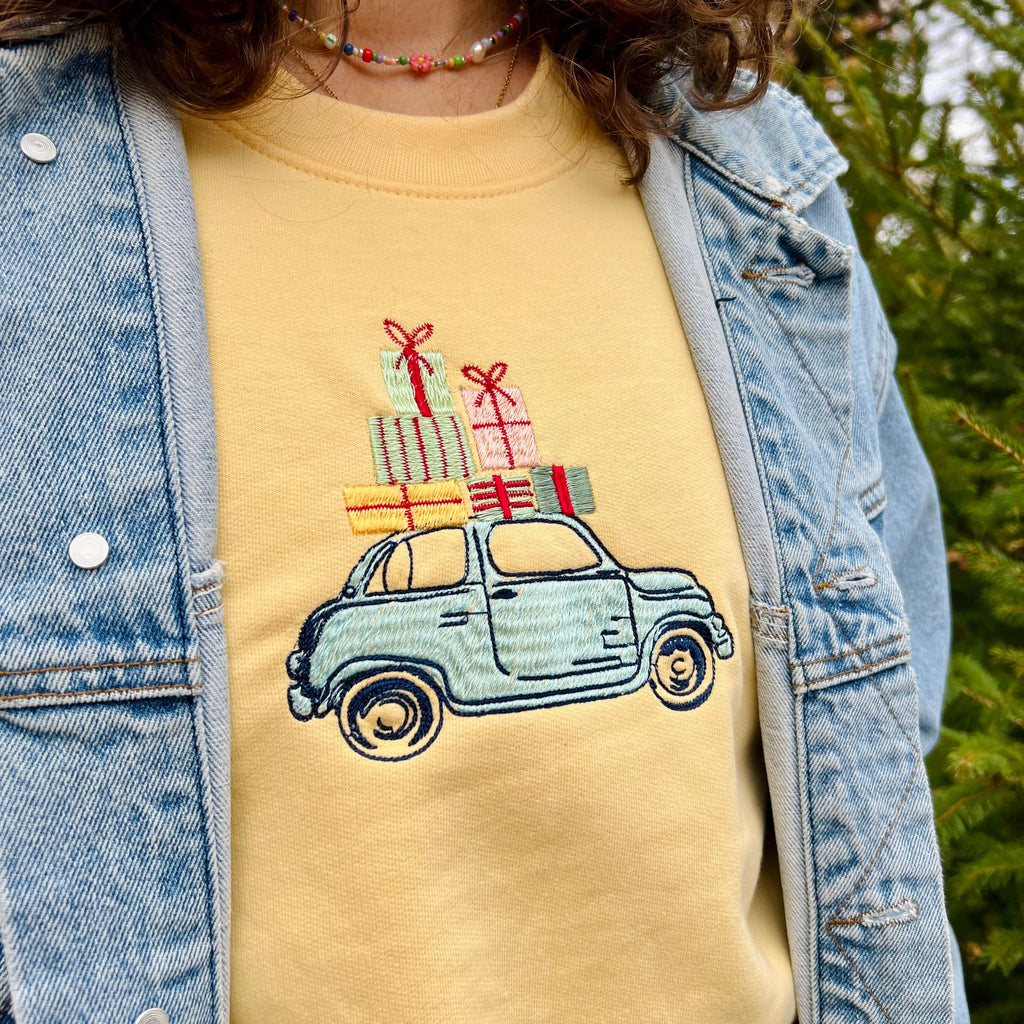Person wearing a yellow shirt with a car and gift box design, outdoors.