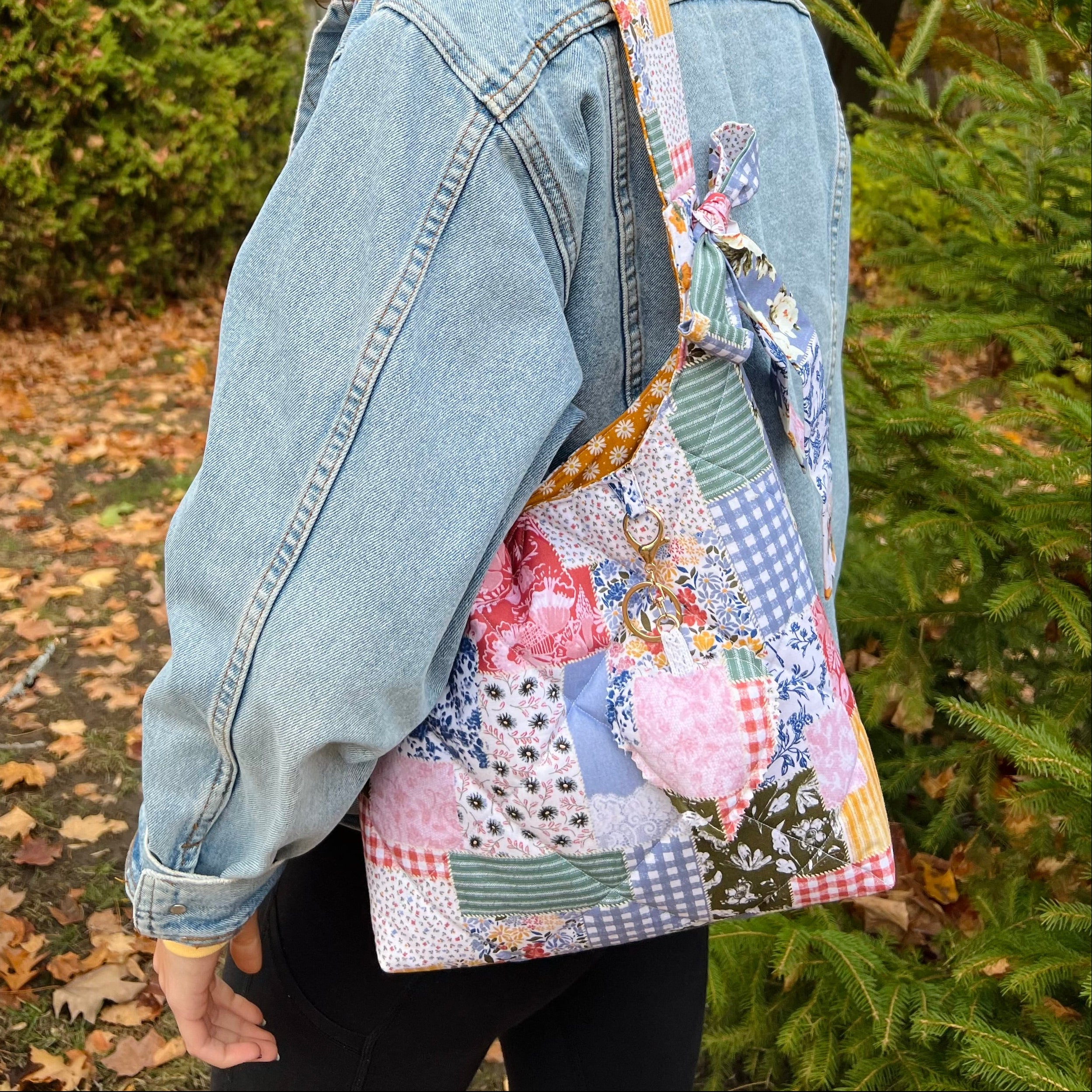 Person wearing a denim jacket and colorful patchwork bag with a dog in an outdoor setting.