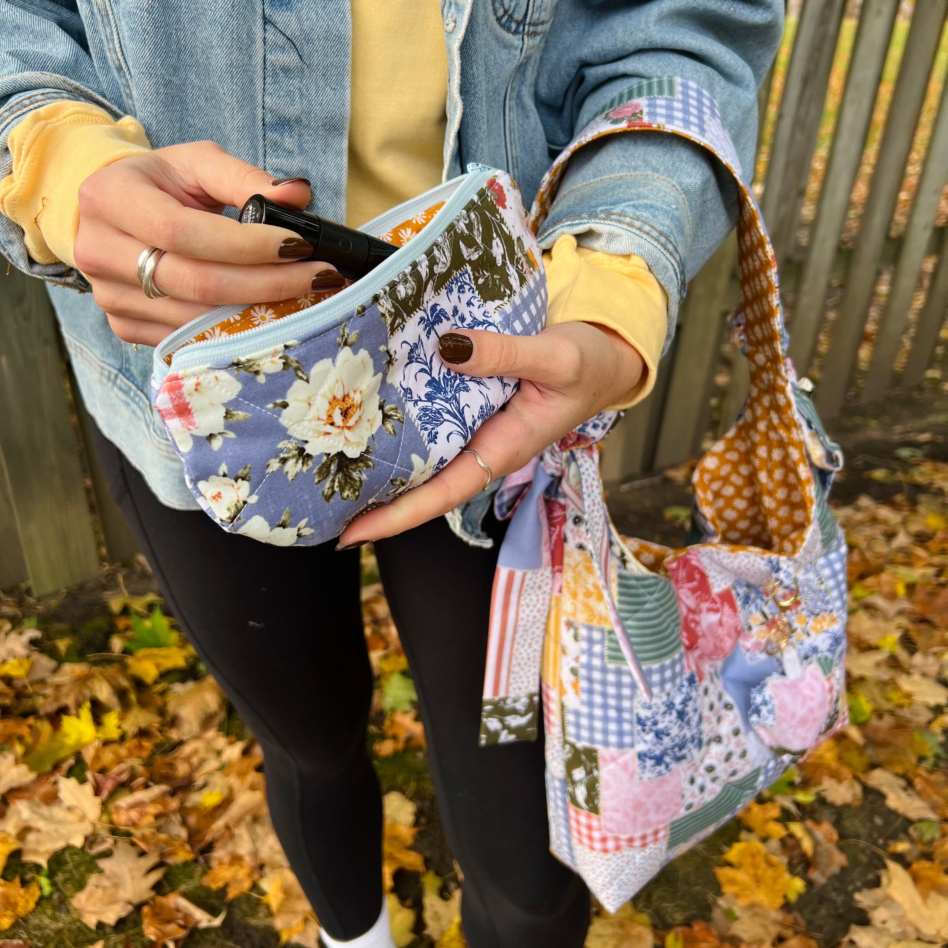 Person holding a floral-patterned pouch with a colorful fabric bag in an outdoor setting.