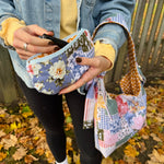 Load image into Gallery viewer, Person holding a floral-patterned pouch with a colorful fabric bag in an outdoor setting.
